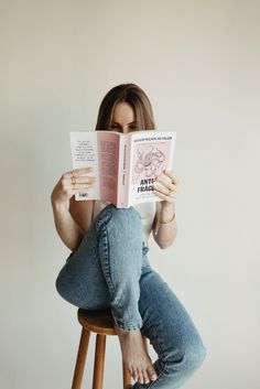 a woman sitting on a stool reading a book