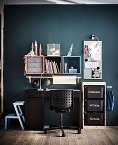 a black chair sitting in front of a desk with bookshelves and pictures on the wall