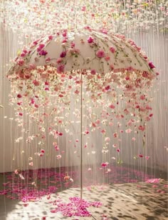 an umbrella with pink flowers hanging from it's sides in front of a white wall