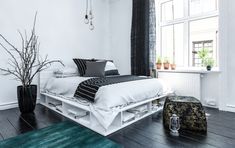 a white bed sitting next to a window in a bedroom on top of a hard wood floor