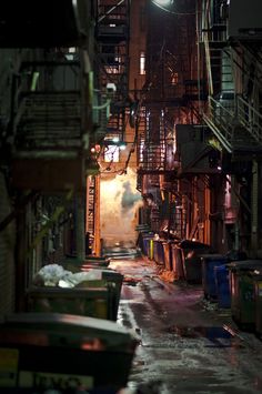 an alley way with lots of trash cans on the floor and stairs to the second floor