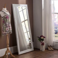 a dress on display in front of a large mirror next to a vase with flowers