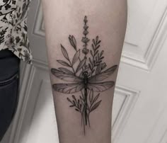 a black and white photo of a dragonfly tattoo on the right arm with flowers