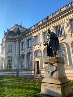 a statue in front of a large building with grass and bushes on the ground below