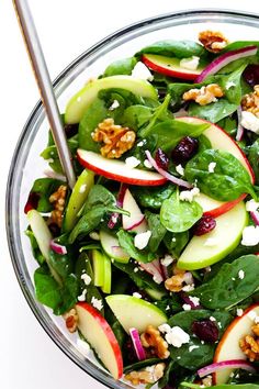 a salad with apples, spinach and walnuts in a glass bowl on a white surface