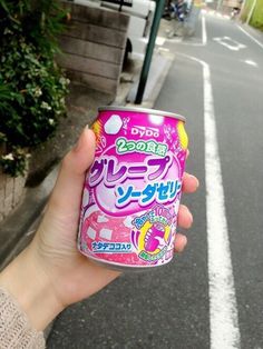 a person holding up a can of soda on the side of a road with buildings in the background