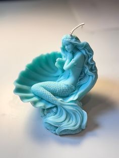 a blue candle with a mermaid sitting on it's side next to a seashell