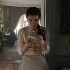 a woman in period clothing looking at a piece of paper