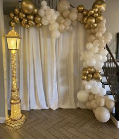 an arch made out of white and gold balloons in front of a staircase with a lamppost