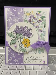 a purple and white card with flowers on it sitting on top of a computer keyboard