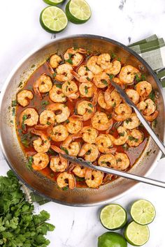 a skillet filled with shrimp and garnished with cilantro, limes and parsley