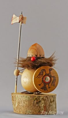 a wooden toy with a hat and flag on it's head sitting on top of a piece of wood