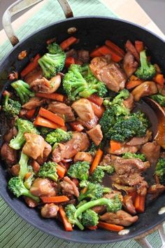 a skillet filled with meat, broccoli and carrots on top of a table