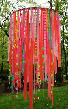 a colorful wind chime in the middle of a grassy area with trees behind it