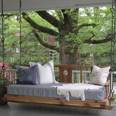 a porch swing bed with pillows on the bottom and sides, in front of a large tree