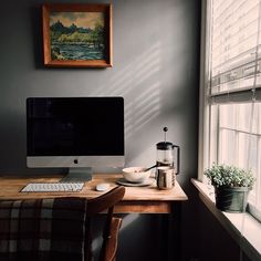 a desktop computer sitting on top of a wooden desk in front of a window next to a potted plant