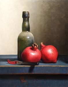 two pomegranates on a table next to a bottle with a knife