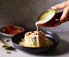 a person pouring milk on top of some food in a black bowl with spoons