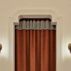 an orange curtain hanging on the side of a white wall next to two sconces