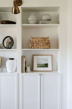 a white book shelf with baskets and pictures on it