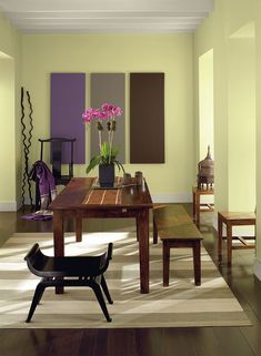 a room with wooden floors and white walls has purple flowers in a vase on the table