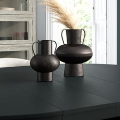 two black vases sitting on top of a wooden table