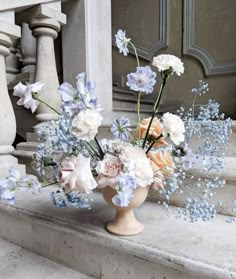 a vase filled with lots of flowers sitting on top of a stone step next to stairs