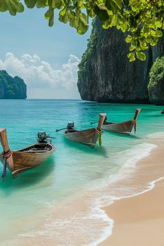 three boats are parked on the beach in front of some cliffs and clear blue water