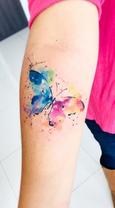 a colorful butterfly tattoo on the right arm and leg, with watercolor paint splatters all over it