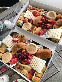 two boxes filled with sandwiches and fruit on top of a wooden table next to plates