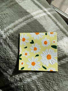 a piece of paper with flowers on it sitting on a bed next to a pillow