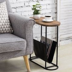 a small table with a magazine rack on it next to a gray couch and white brick wall