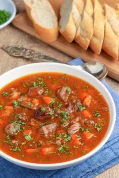 a bowl of soup with meat and carrots on a blue towel next to bread