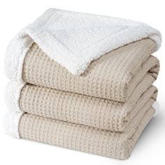 three blankets stacked on top of each other in beige and white colors, with one folded up to the side