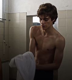 a shirtless man standing in a bathroom next to a sink and towel hanging on the wall