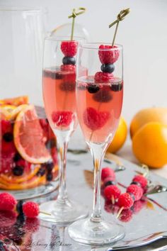 two wine glasses filled with raspberries and lemons on a silver platter