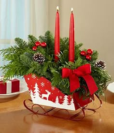 a christmas centerpiece with red candles and pine cones in it on a wooden table