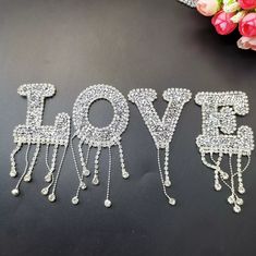 the word love spelled with crystal beads on a black surface next to flowers and a bouquet