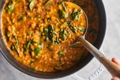 a person holding a spoon full of red lentils and spinach soup in a pot