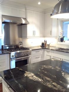 a kitchen with white cabinets and black granite counter tops, stainless steel appliances and an island in the middle