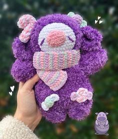 a hand holding a purple teddy bear wearing a knitted hat and mittens