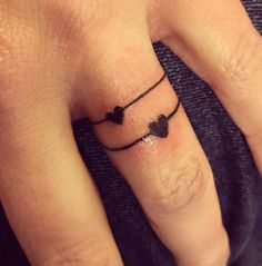 a woman's finger with two hearts on it and a small black heart tattoo