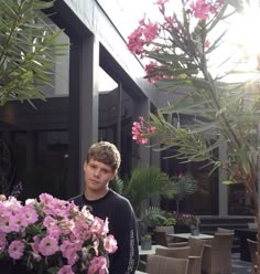 a young man standing next to a potted plant with pink flowers in front of him