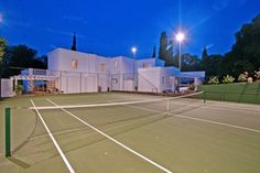 a tennis court with a white building in the background at night, lit up by street lights