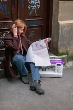 a woman sitting on the ground talking on her cell phone and holding a paper bag