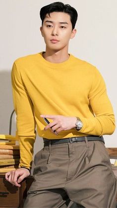 a young man in a yellow sweater is sitting on a chair and looking at his cell phone