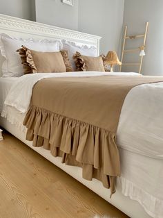 a white bed topped with lots of pillows next to a wooden chair and lamp on top of a hard wood floor