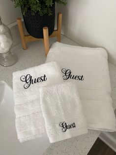 two white towels sitting on top of a bathroom counter next to a potted plant