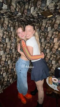 two young women hugging each other in front of a wallpapered room with skulls