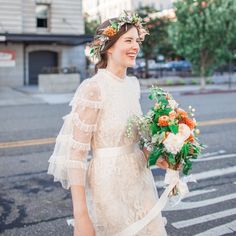 a woman is walking down the street with flowers in her hair and holding a bouquet